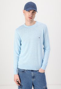 Svetlo modra dolga majica z dolgimi rokavi in okroglo ovratnikom, z rebrastimi manšetami, v kombinaciji z denim kratkimi hlačami. Ima majhen logotip na prsih.