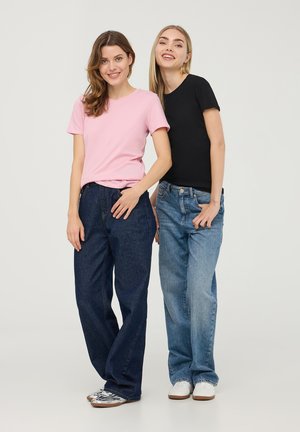 Dwie osoby stoją obok siebie, jedna w różowej koszulce i ciemnoniebieskich dżinsach, a druga w czarnej koszulce i jasnoniebieskich dżinsach.