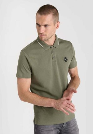 Olijfgroene polo met een kraag, drie knopen aan de voorkant, witte accentstiksel en een ronde logo op de linkerkant van de borst. Korte mouwen.