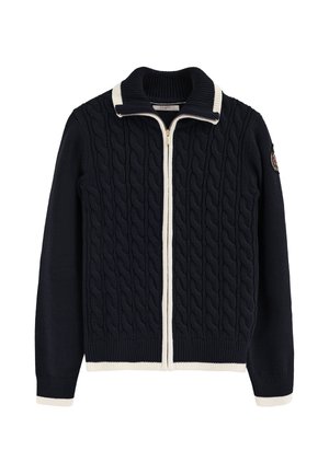 Sudadera azul marino de punto grueso con cremallera, con ribete blanco en el cuello, los puños y el dobladillo, que presenta un cuello alto acanalado y un parche en la manga izquierda.