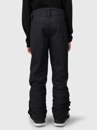 Person som har på seg svarte vanntette bukser og svarte sko, står med ryggen til kameraet på en ensfarget bakgrunn.