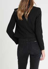 Musta lyhyt bleiseri, jossa on istuva leikkaus. Yhdistetty mustiin korkeavyötäröisiin farkkuihin, joissa on kaksi takataskua ja kaarevat saumat.