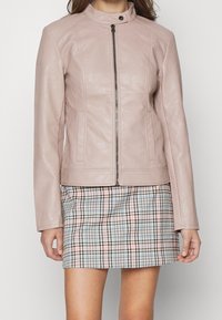 Giacca in pelle rosa chiaro con colletto alla coreana, zip frontale e due tasche laterali, abbinata a una minigonna scozzese con colori pastello.