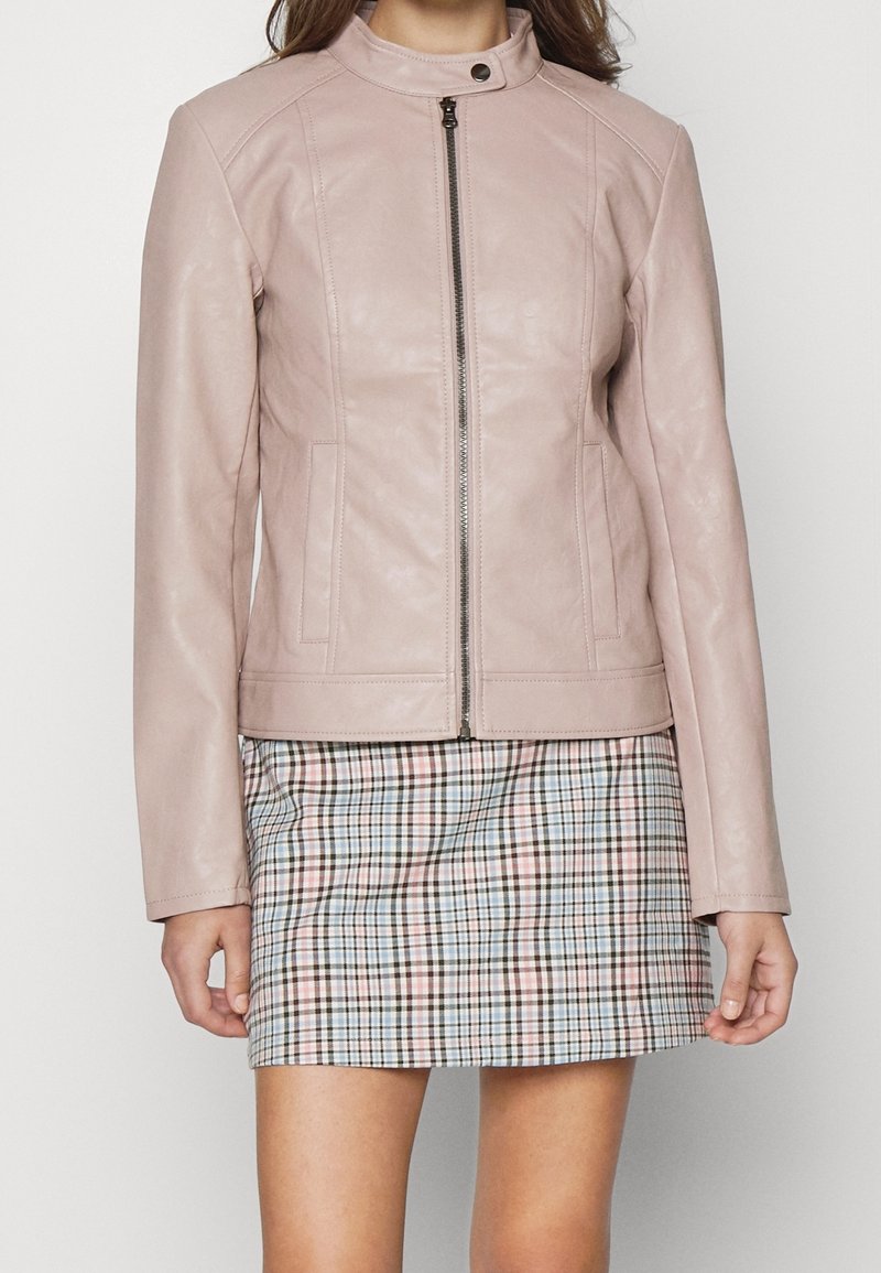 Giacca in pelle rosa chiaro con colletto alla coreana, zip frontale e due tasche laterali, abbinata a una minigonna scozzese con colori pastello.