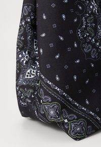 Close-up van de hoek van een zwart stoffen tas met witte en groene paisley- en bloempatronen op de gestructureerde stof.