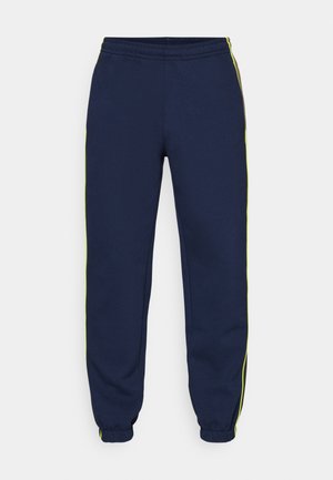 Pantaloni della tuta blu navy con vita elasticizzata, polsini affusolati e strisce laterali contrastanti di colore verde neon. Realizzati in una texture di tessuto liscia.