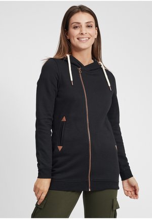 Haut zippé noir avec un col bénitier, cordons de couleur crème, fermeture éclair en cuivre et accents triangulaires marron au niveau des poches. Matière douce, design ajusté.