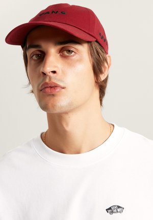 Maroon cap with black "VANS" logo, worn with a white T-shirt featuring a small black "VANS Off the Wall" logo on the chest.