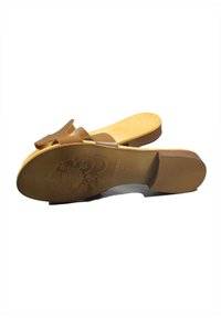 Sandalo slide marrone con una fascia larga e un dettaglio a fiocco. Materiale superiore liscio, soletta sagomata e suola testurizzata con motivo floreale.