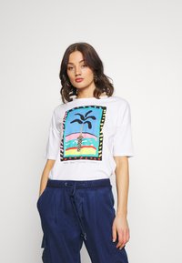 Camiseta blanca con un gráfico colorido de una palmera en un marco rectangular con acentos en negro y multicolores, hecha de tela de algodón.