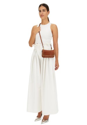 Top bianco senza maniche e pantaloni bianchi a gamba larga, abbinati a una borsa a tracolla in pelle marrone con dettagli dorati e una superficie liscia.