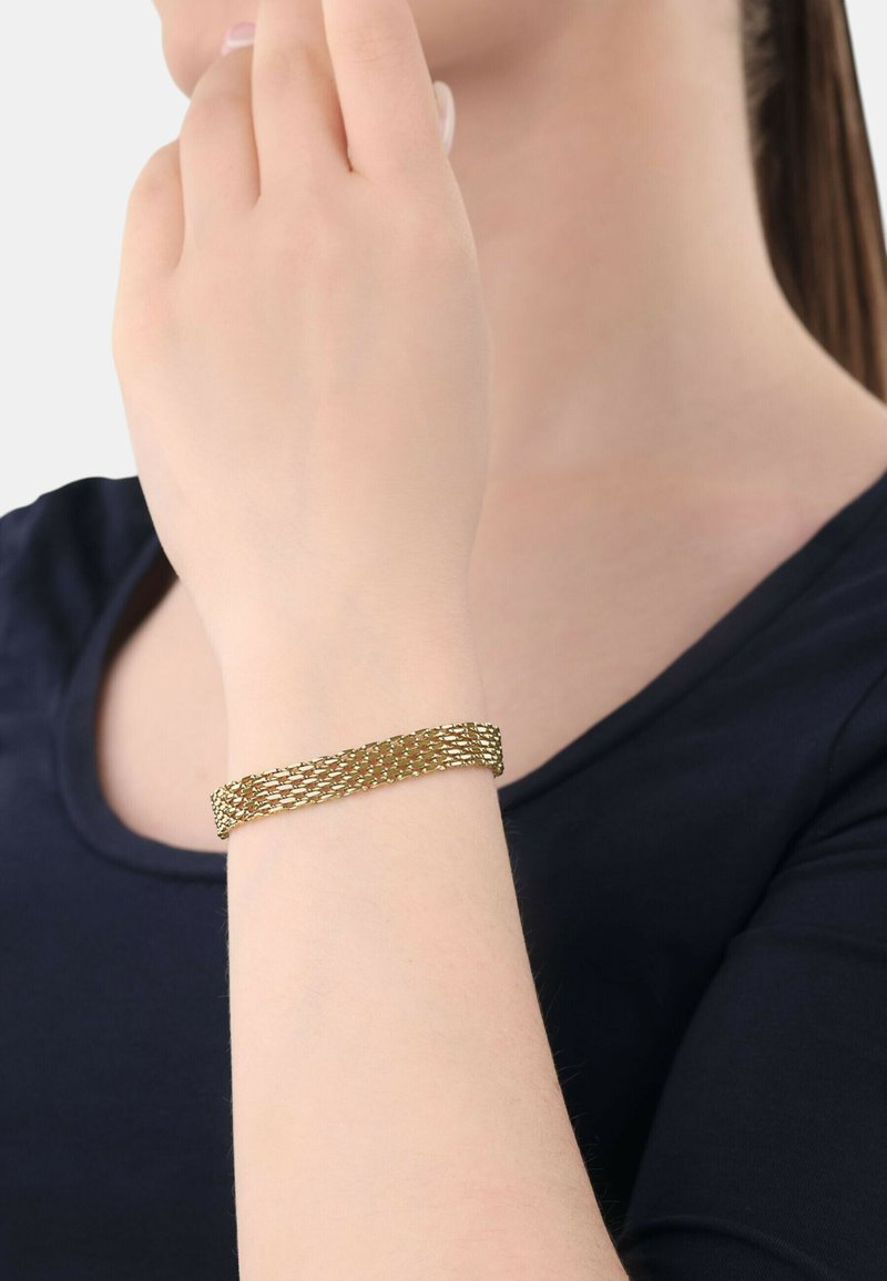 Pulsera de metal en tono dorado con un diseño trenzado y un acabado texturizado, llevada en una muñeca con un tono de piel suave.