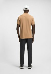 Brun polo-shirt med korta ärmar, vit krage, i kombination med mörkgrå byxor och svarta skor, sedd bakifrån.