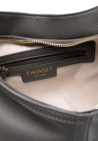 Interno di una borsa in pelle nera con rivestimento in tessuto beige, una tasca con zip e etichetta dorata "TWINSET MILANO".