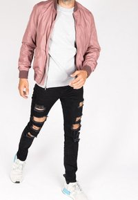 Chaqueta bomber de color rosa claro sobre una camiseta gris, combinada con vaqueros negros desgarrados y zapatillas blancas con detalles en azul.