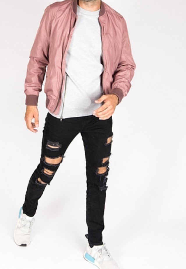 Chaqueta bomber de color rosa claro sobre una camiseta gris, combinada con vaqueros negros desgarrados y zapatillas blancas con detalles en azul.
