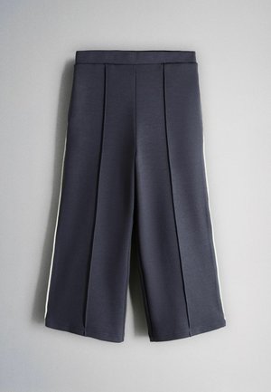 Námornícke široké nohavice s prednými záhybmi a bielymi bočnými pruhmi, položené na svetlosivom pozadí.