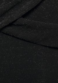 Černá tkanina s texturovaným povrchem, zdobená rozptýlenými stříbrnými kovovými tečkami, vytvářejícími jemný efekt lesku.