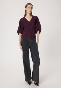 Plum bluse med pufærmer og V-hals, parret med høj talje sorte vidde jeans og sorte spidse hæle. Glat stoftekstur.
