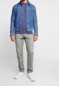 Veste en jean bleu clair, associée à un sweat-shirt violet et un pantalon gris texturé. Des baskets blanches complètent le look.