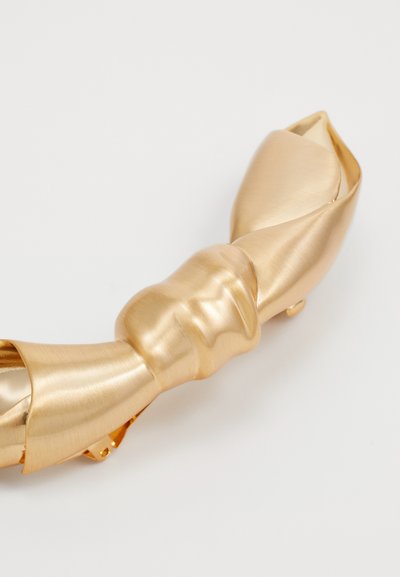 Goudkleurige haaraccessoire met een gedraaide vorm, afgewerkt met zowel een gladde als een geborstelde textuur, en toont elegante lijnen en een glanzend oppervlak.