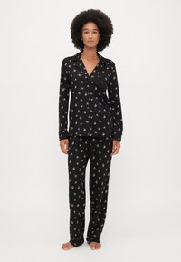Set de pijama negru cu o cămașă cu nasturi, decorată cu un model floral și pantaloni asortați. Material moale, cu o croială lejeră și detaliu de buzunar la piept.