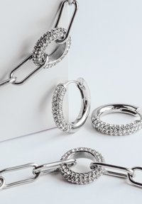 Gioielli in argento con orecchini a cerchio e catena. Gli orecchini sono adornati con gemme trasparenti, che mostrano una finitura lucida e brillante.