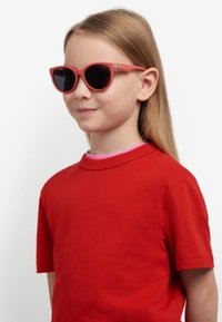 T-shirt rosso a maniche corte con collo rosa, abbinato a occhiali da sole rotondi fucsia con lenti nere.