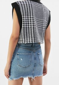 Černo-bílý kostkovaný crop top bez rukávů, spárovaný s vybledlou denimovou mini sukní s ošoupanými okraji a zadními kapsami.