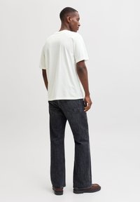 Hvid bomulds-t-shirt med løs pasform, kombineret med løstsiddende mørke denimjeans. Modellen står sideværts med en neutral baggrund.