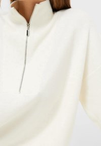 Lichtcrème zip-nek pullover, ribbelstructuur, ontspannen pasvorm, iets oversized mouwen, zilveren ritssluiting, vlakke naad bij de kraag.