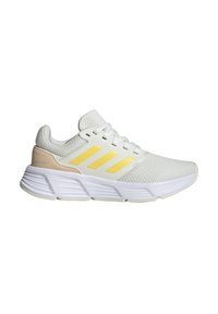 Scarpa sportiva bianca con strisce gialle e accenti beige chiaro, realizzata in tessuto texturizzato con collo imbottito e suola ammortizzata.
