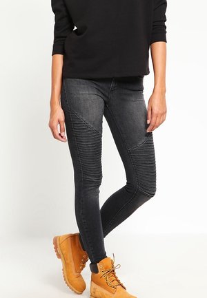 Los pantalones vaqueros ajustados de mezclilla negra presentan un detallado de relieve texturizado en la parte delantera, complementados por botas de tobillo con cordones en un tono marrón anaranjado.