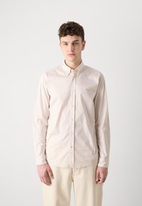 Camicia a maniche lunghe di colore chiaro con sottili righe verticali. Collo button-down, bottoni sul frontale e un sottile marchio sul petto. Texture liscia.