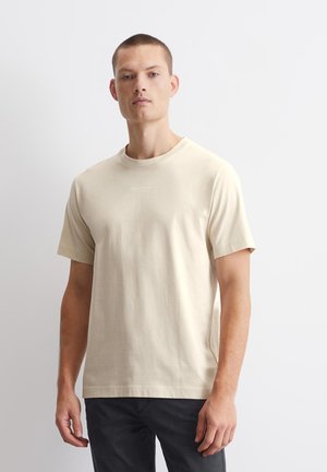 Tricou din bumbac bej, cu guler rotund și mâneci scurte, având detalii minime ale logo-ului pe piept și o croială lejeră.