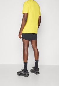 Keltainen puuvillainen t-paita, mustat urheilushortsit, mustat Nike-sukat ja mustat kengät. Korostaa rentoa, urheilullista designia ja mukavaa istuvuutta.