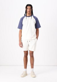 Camiseta de manga corta raglán en gris y navy combinada con pantalones cortos ligeros y texturizados. Presenta bolsillos frontales y zapatillas bajas.