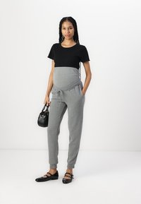 Maternitātes apģērbs ar melnu īsām piedurknēm augšdaļu un pelēkiem sporta biksēm ar stinguma jostu, brīvu piegriezumu un sānu kabatām.