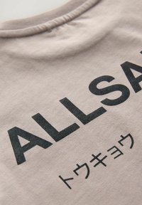 Pelēkas T-krekls ar melnu drukātu tekstu "ALLSA" zem kura ir japāņu rakstzīmes. Mīksts audums ar noapaļotu apkakli un redzamām vīlēm.