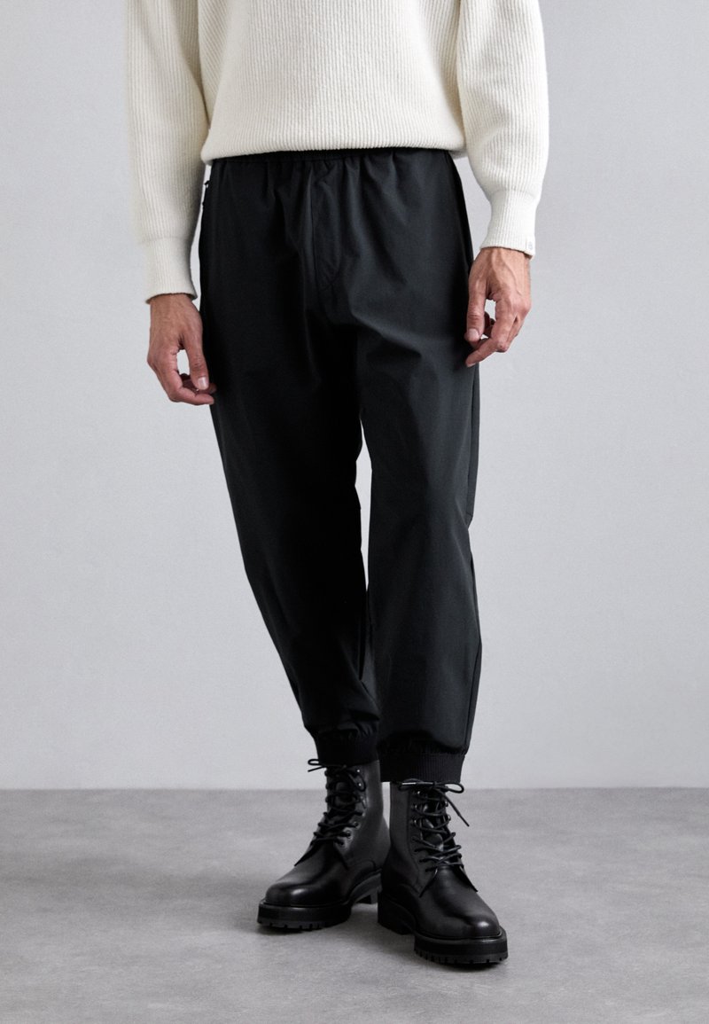 Mustat, joustovyötäröiset jogger-housut kapeutuvilla varrella, yhdistettynä mustiin nauhakengiin. Asusteena on ribattu valkoinen neule.