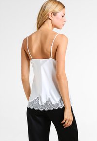 White satin camisole with thin straps, featuring a scalloped lace hem in gray. Smooth texture, elegant design, and fitted cut.