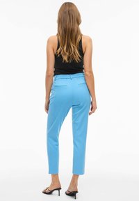 Lyseblå skreddersydde bukser med elastisk midjebånd og baklommer, stylet med en tettsittende svart tanktopp og svarte hæler med stropper.