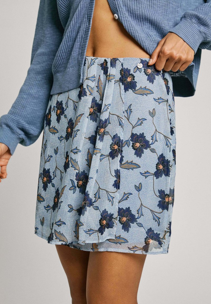 Spódnica w kwiaty w jasnoniebieskim kolorze z granatowymi i brzoskwiniowymi kwiatami. Plisowany fason z detalem w postaci guzika w talii. Wykonana z lekkiego materiału.