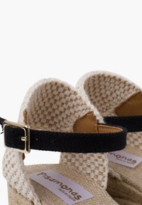 Geweven beige espadrillesandalen met een zwarte stoffen enkelband en een metallic sluiting. Natuurlijke vezelzool met zichtbaar merklabel.