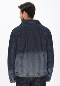 Sötétkék farmerdzseki, amely fokozatosan világosabb árnyalatokba megy át. Klasszikus gallérral és gombos mandzsettákkal rendelkezik, enyhén megkopott textúrával.