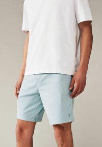 Pantaloni scurți de culoare bleu deschis, confecționați dintr-un amestec de bumbac, cu talie plată, buzunare laterale și un mic logo pe marginea stângă. Tăiati peste genunchi.