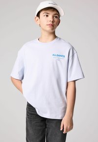 Balta medvilninė marškinėliai su trumpomis rankovėmis, su mėlynu "ALLSAINTS" logo. Užsidėta su tamsiais, tekstūriniais džinsais ir derančiu baltu kepurėliu.