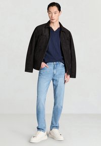 Giacca in camoscio scuro, maglietta a V blu navy, jeans azzurri, scarpe da ginnastica bianche. Design semplice con due tasche frontali sulla giacca.