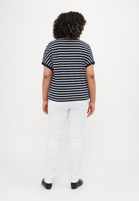 Top a righe crema e blu navy a maniche corte abbinato a pantaloni bianchi. Scarpe nere. Orlo curvo visibile e vestibilità rilassata in tessuto morbido.