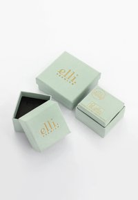 Des boîtes-cadeaux vert menthe avec des lettres dorées, présentant une forme carrée et une texture lisse. Une boîte est partiellement ouverte, révélant un intérieur noir.
